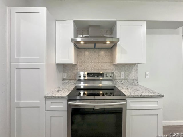 kitchen with wall chimney range hood, stainless steel electric stove, and white cabinets