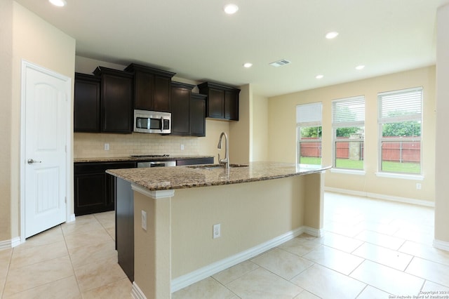 kitchen with sink, light stone countertops, a kitchen island with sink, and decorative backsplash