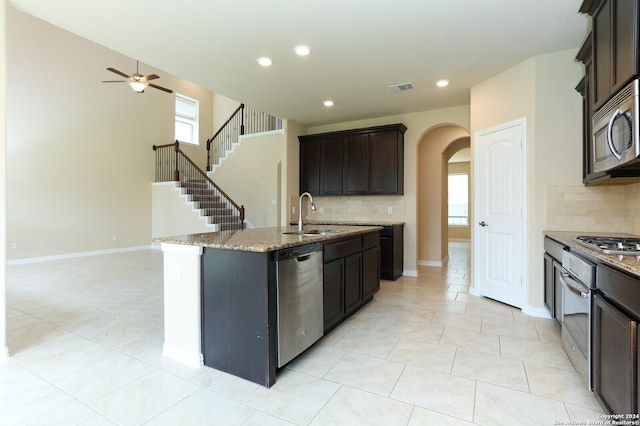 kitchen featuring an island with sink, sink, light tile patterned floors, stainless steel appliances, and dark brown cabinets