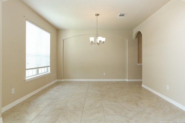 tiled spare room with a chandelier