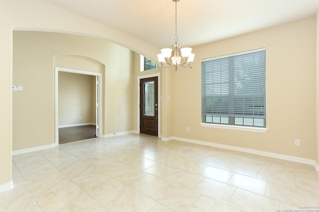 tiled spare room with a notable chandelier