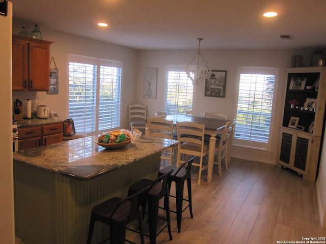 kitchen with dark stone countertops, decorative light fixtures, a breakfast bar, and light wood-type flooring