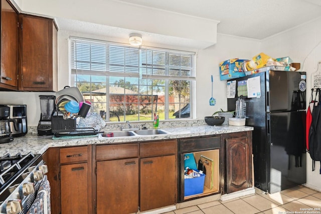 kitchen with sink, stainless steel stove, light tile patterned floors, black refrigerator, and ornamental molding