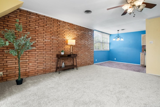 unfurnished living room featuring brick wall, carpet floors, and ceiling fan with notable chandelier