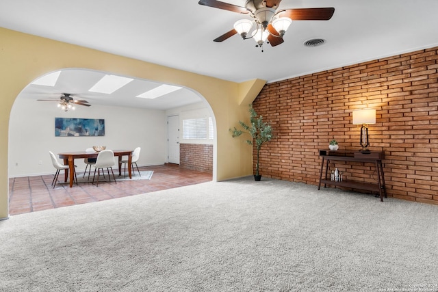 living room with brick wall, light carpet, ceiling fan, and a skylight