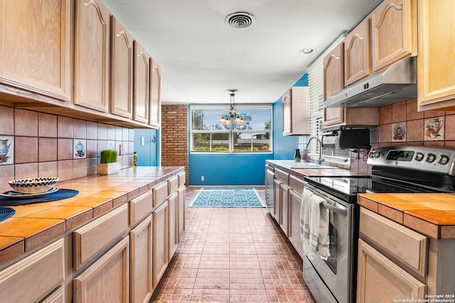 kitchen featuring sink, appliances with stainless steel finishes, hanging light fixtures, decorative backsplash, and tile countertops