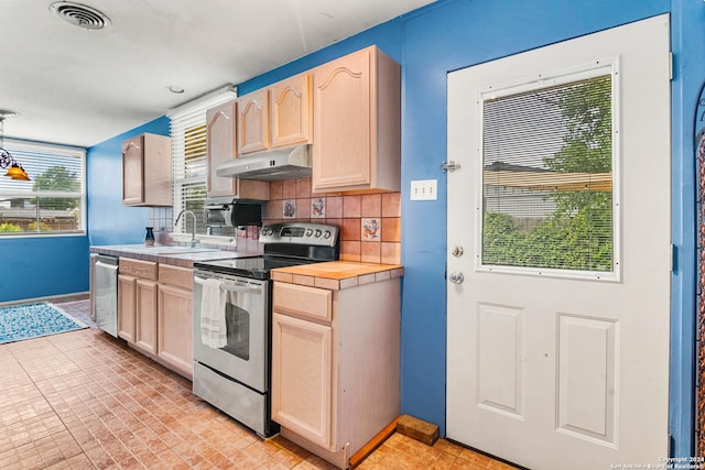 kitchen featuring appliances with stainless steel finishes, tile countertops, light brown cabinetry, decorative light fixtures, and sink