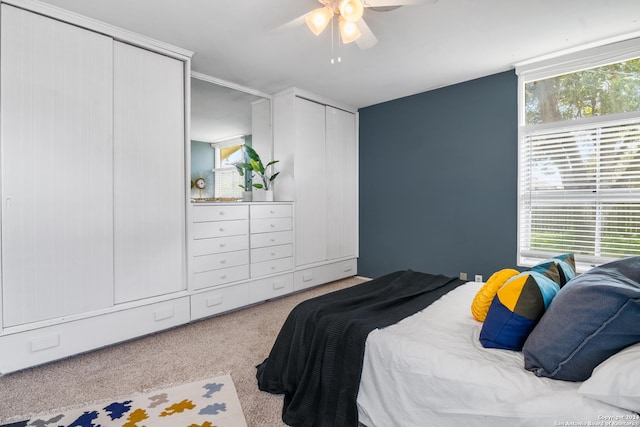 bedroom with ceiling fan, light carpet, and two closets