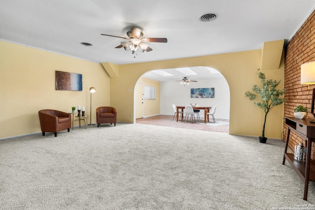 living area featuring light colored carpet, ceiling fan, and brick wall