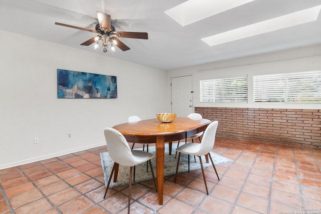 tiled dining space with brick wall, ceiling fan, and a skylight