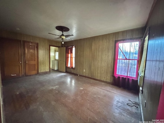 spare room with ceiling fan, concrete flooring, and wood walls