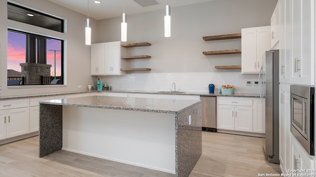 kitchen featuring white cabinetry, stainless steel appliances, a center island, and light stone counters