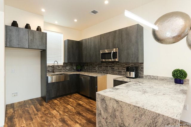 kitchen featuring dark brown cabinetry, sink, tasteful backsplash, dark hardwood / wood-style floors, and stainless steel appliances