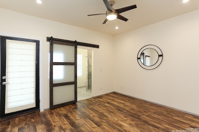 unfurnished room featuring ceiling fan, a barn door, and dark hardwood / wood-style flooring