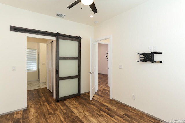 unfurnished bedroom with dark hardwood / wood-style floors, ceiling fan, and a barn door