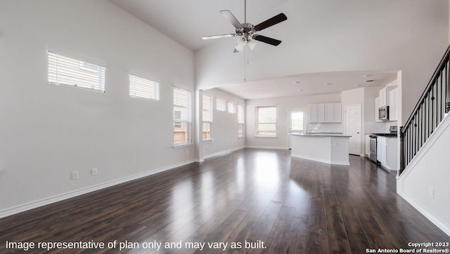 unfurnished living room with ceiling fan, dark hardwood / wood-style floors, and a high ceiling