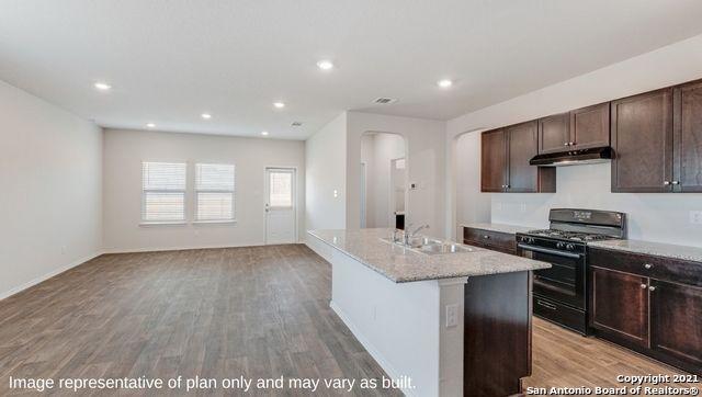 kitchen with sink, light hardwood / wood-style floors, light stone countertops, a center island with sink, and black range with gas cooktop