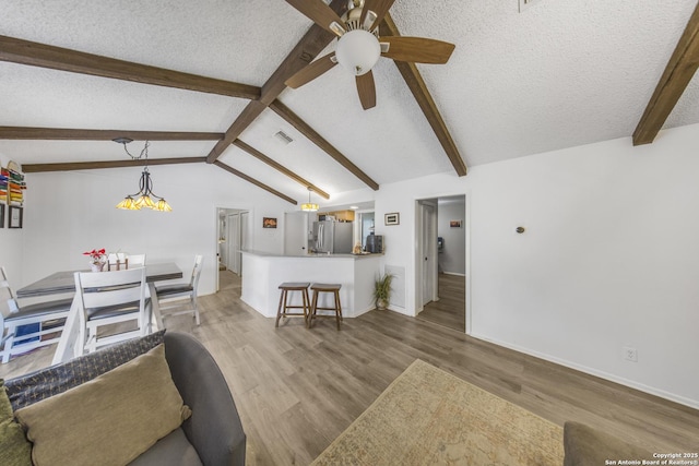 living room featuring vaulted ceiling with beams, ceiling fan, a textured ceiling, and light wood-type flooring