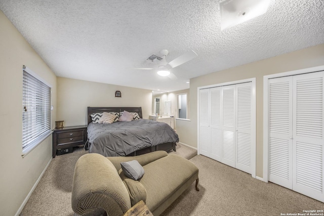 carpeted bedroom with multiple windows, two closets, a textured ceiling, and ceiling fan