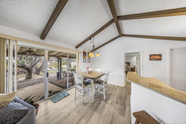 dining area featuring hardwood / wood-style flooring, vaulted ceiling with beams, ceiling fan with notable chandelier, and a textured ceiling