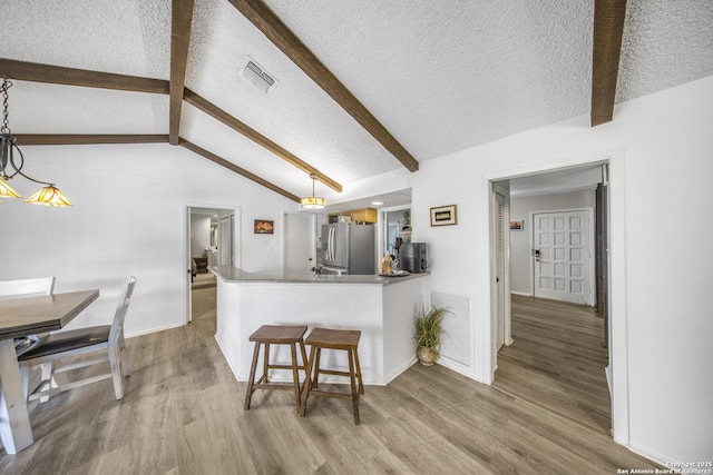 kitchen with a kitchen bar, lofted ceiling with beams, stainless steel fridge with ice dispenser, light wood-type flooring, and kitchen peninsula