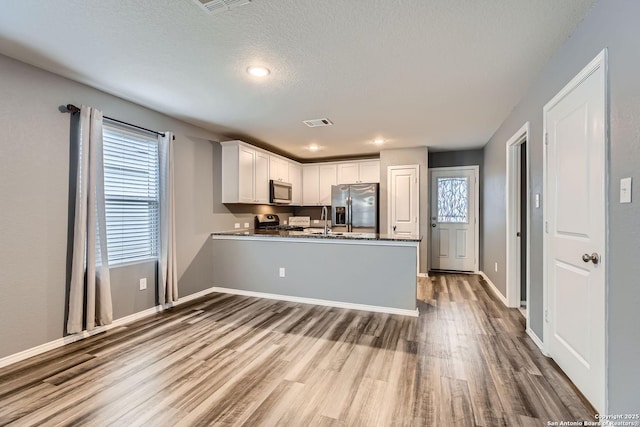 kitchen featuring sink, wood-type flooring, appliances with stainless steel finishes, kitchen peninsula, and white cabinets