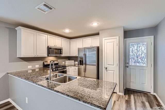 kitchen with appliances with stainless steel finishes, kitchen peninsula, dark stone counters, hardwood / wood-style floors, and white cabinets