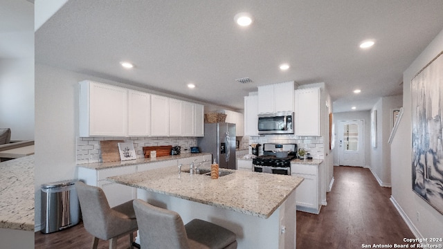 kitchen with light stone countertops, white cabinetry, appliances with stainless steel finishes, and a center island with sink