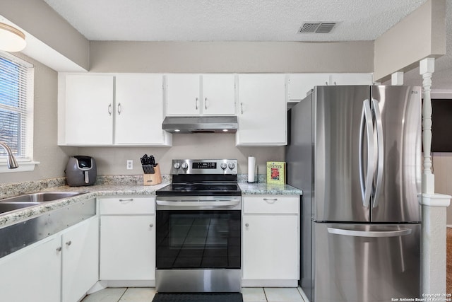 kitchen with sink, light tile patterned floors, stainless steel appliances, a textured ceiling, and white cabinets