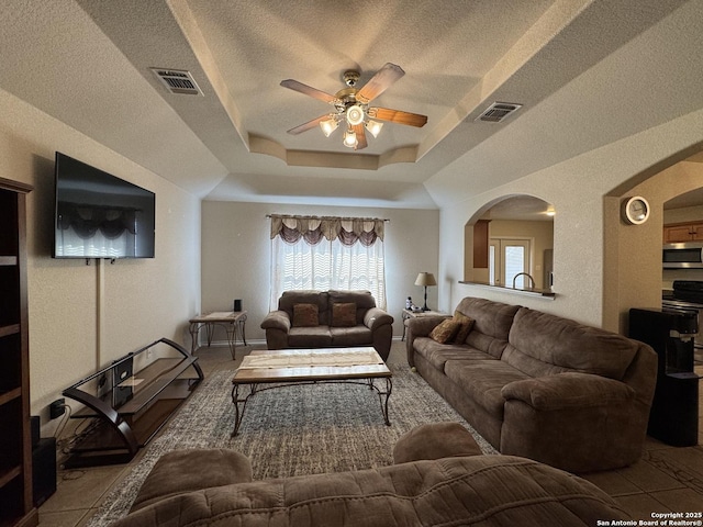 living room with ceiling fan, a textured ceiling, and a tray ceiling