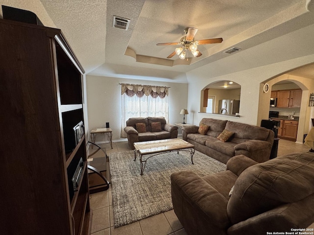 tiled living room featuring ceiling fan, a raised ceiling, and a textured ceiling