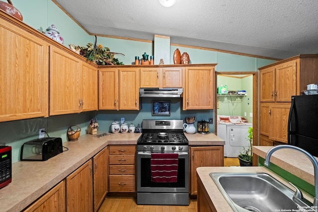 kitchen with vaulted ceiling, sink, stainless steel gas range oven, a textured ceiling, and washing machine and dryer