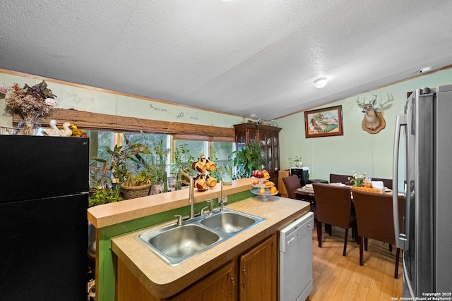 kitchen with lofted ceiling, stainless steel refrigerator, dishwasher, a center island with sink, and black fridge