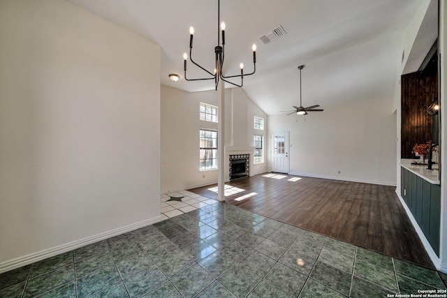 unfurnished living room featuring dark tile patterned flooring, ceiling fan with notable chandelier, and high vaulted ceiling