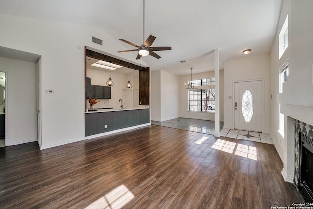 unfurnished living room featuring dark hardwood / wood-style flooring, sink, ceiling fan with notable chandelier, and high vaulted ceiling