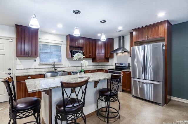 kitchen with pendant lighting, sink, stainless steel appliances, a kitchen island, and wall chimney exhaust hood