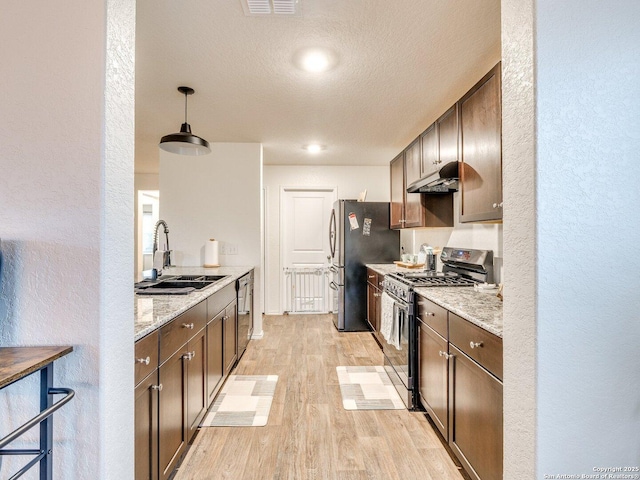 kitchen with pendant lighting, sink, stainless steel appliances, light stone countertops, and light hardwood / wood-style flooring