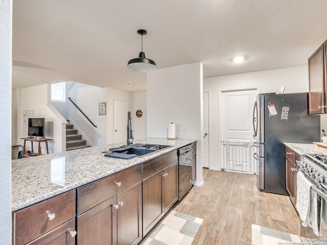 kitchen featuring sink, light hardwood / wood-style flooring, appliances with stainless steel finishes, hanging light fixtures, and light stone countertops