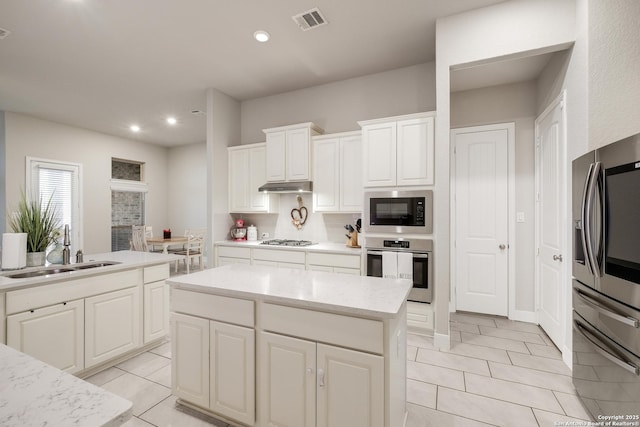 kitchen with sink, appliances with stainless steel finishes, white cabinetry, a center island, and decorative backsplash