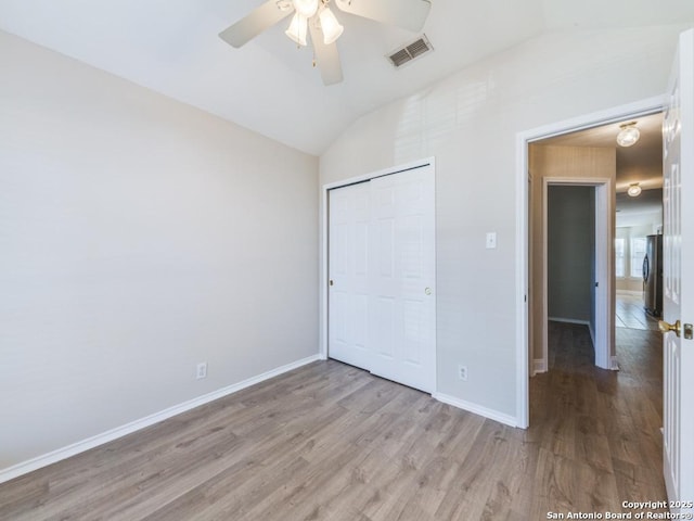 unfurnished bedroom with stainless steel refrigerator, light hardwood / wood-style floors, vaulted ceiling, and a closet