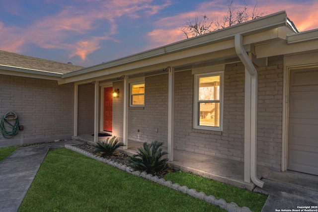 exterior entry at dusk with a porch, a garage, and a yard