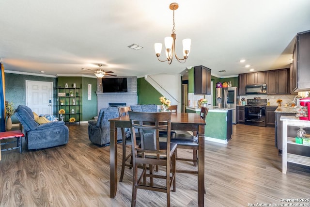 dining area featuring crown molding, ceiling fan with notable chandelier, a fireplace, and light wood-type flooring