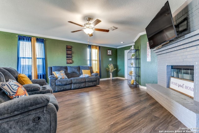 living room featuring a textured ceiling, ornamental molding, dark hardwood / wood-style flooring, ceiling fan, and a fireplace