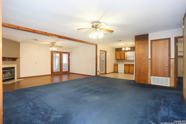 unfurnished living room with ceiling fan with notable chandelier, a textured ceiling, and dark colored carpet