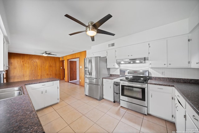 kitchen featuring appliances with stainless steel finishes, light tile patterned floors, white cabinets, and wooden walls