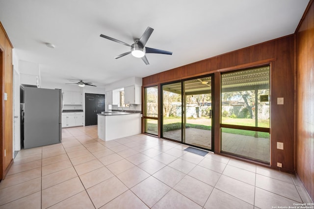 unfurnished living room with light tile patterned floors, ceiling fan, and wood walls