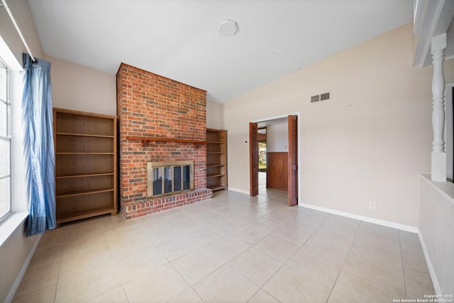 unfurnished living room featuring lofted ceiling, a brick fireplace, a wealth of natural light, and light tile patterned flooring