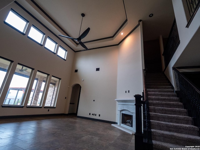 unfurnished living room featuring a raised ceiling, a towering ceiling, and ceiling fan