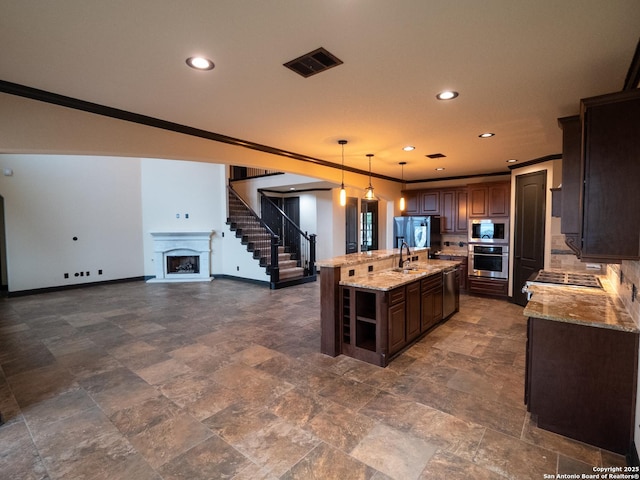 kitchen featuring crown molding, appliances with stainless steel finishes, dark brown cabinets, decorative light fixtures, and a large island with sink