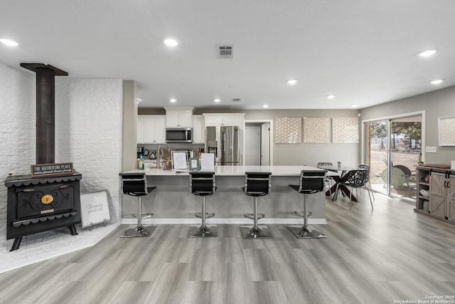 kitchen featuring light hardwood / wood-style floors, appliances with stainless steel finishes, white cabinets, and a kitchen bar